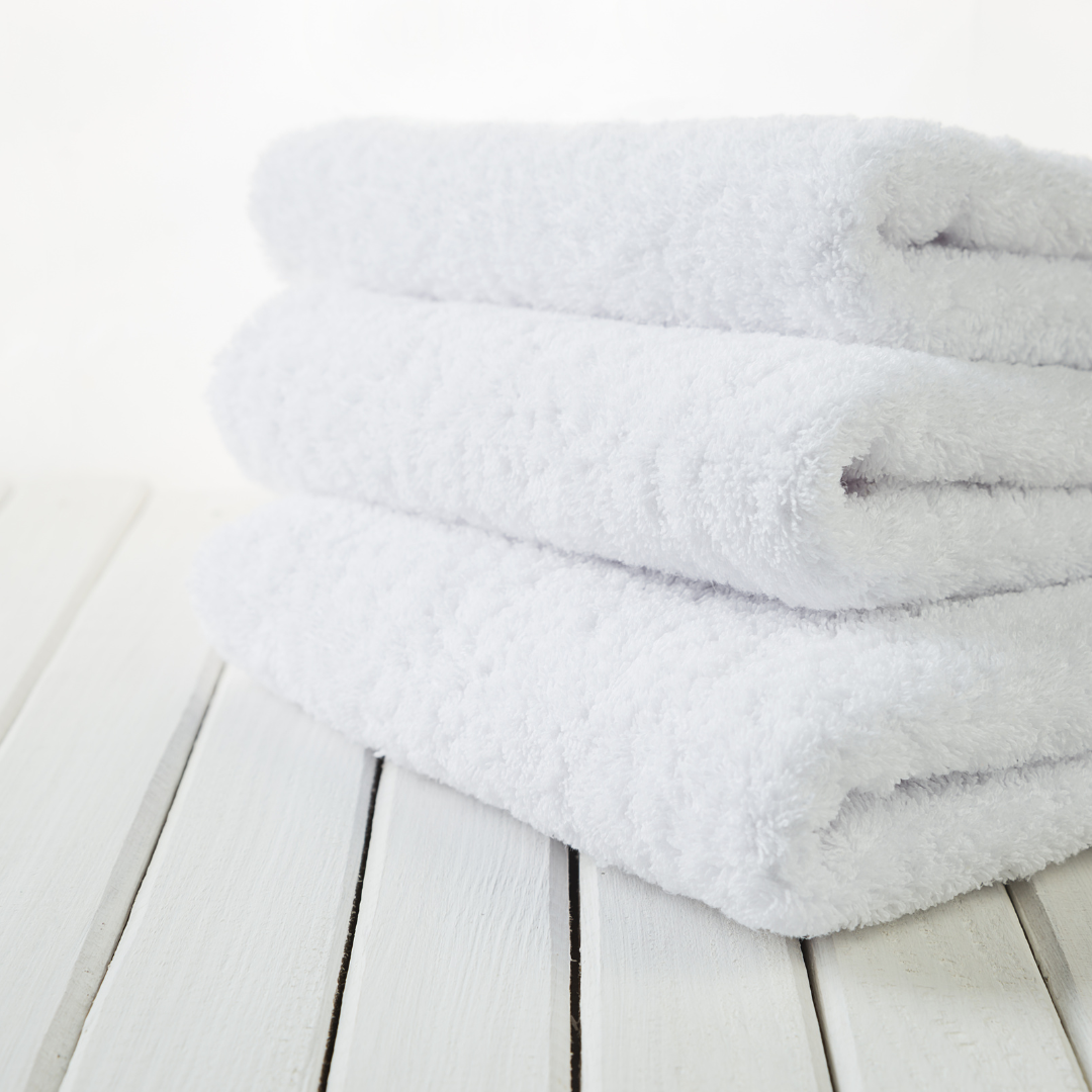 A neatly folded organic cotton towel in a soft, natural shade, with a smooth, plush texture. The towel lies on a wooden surface, radiating a sense of warmth and luxury. Nearby, a hint of greenery adds a touch of nature, highlighting the towel’s eco-friendly, sustainable origins, perfect for a relaxing, spa-like self-care experience