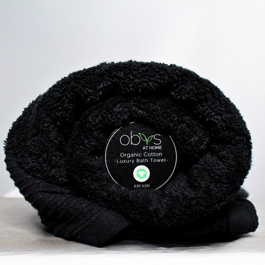 A neatly folded organic cotton towel in a soft, natural shade, with a smooth, plush texture. The towel lies on a wooden surface, radiating a sense of warmth and luxury. Nearby, a hint of greenery adds a touch of nature, highlighting the towel’s eco-friendly, sustainable origins, perfect for a relaxing, spa-like self-care experience
