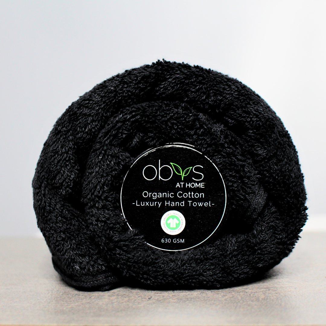 A neatly folded organic cotton towel in a soft, natural shade, with a smooth, plush texture. The towel lies on a wooden surface, radiating a sense of warmth and luxury. Nearby, a hint of greenery adds a touch of nature, highlighting the towel’s eco-friendly, sustainable origins, perfect for a relaxing, spa-like self-care experience
