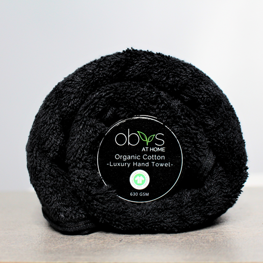 A neatly folded organic cotton towel in a soft, natural shade, with a smooth, plush texture. The towel lies on a wooden surface, radiating a sense of warmth and luxury. Nearby, a hint of greenery adds a touch of nature, highlighting the towel’s eco-friendly, sustainable origins, perfect for a relaxing, spa-like self-care experience