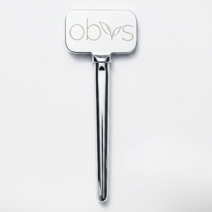 A polished silver metal hair tool with a rectangular head engraved with the brand name 'obvs' and a small leaf motif, shown on a clean white background.