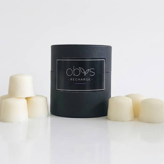 Black container labeled 'obvs' with white cylindrical products on a light gray background wax melts