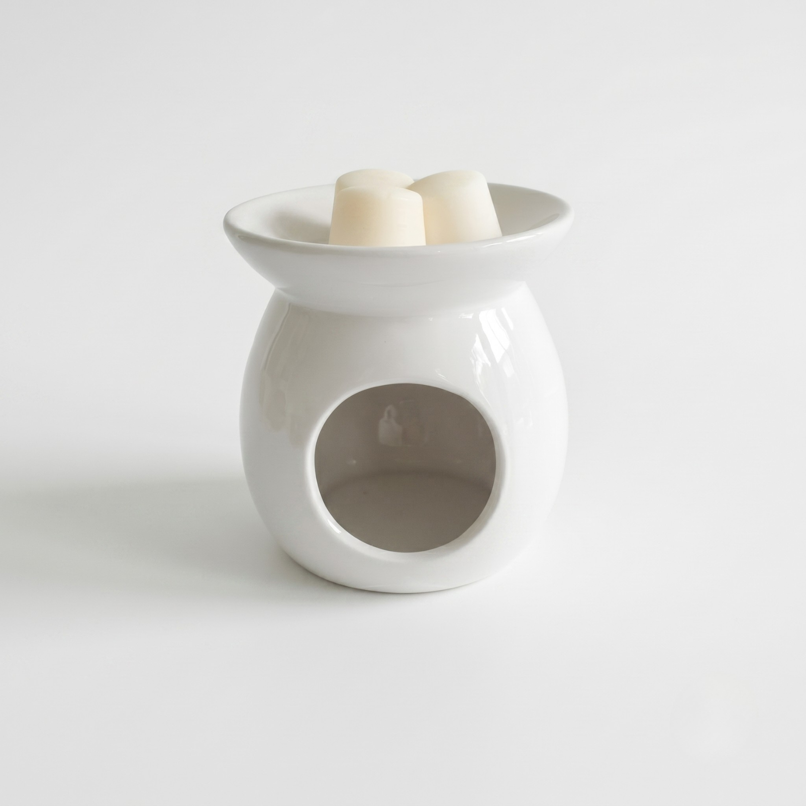 White ceramic wax warmer with a candle on a light gray background