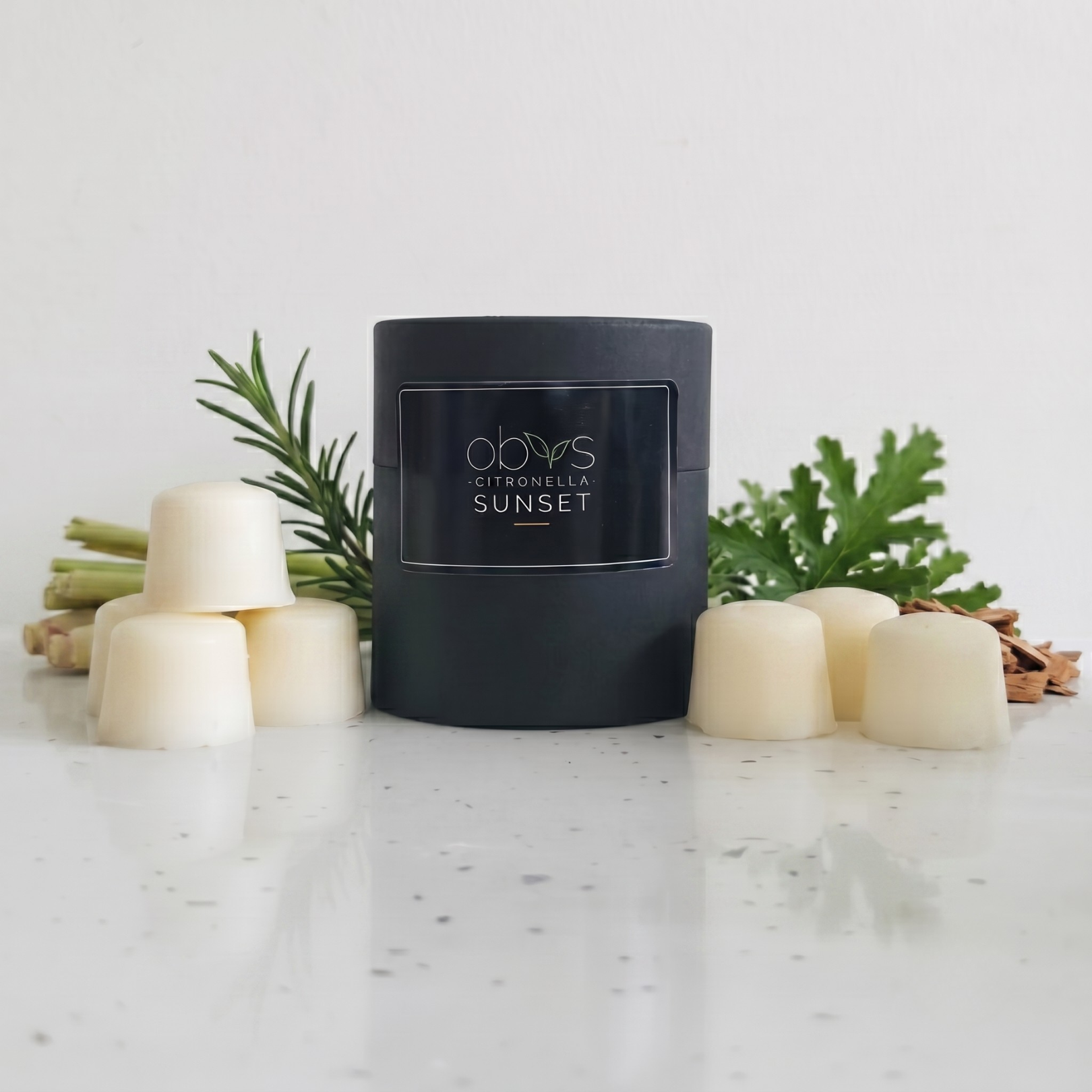 Black wax melt container labeled 'Citronella Sunset' on a marble surface with decorative elements.