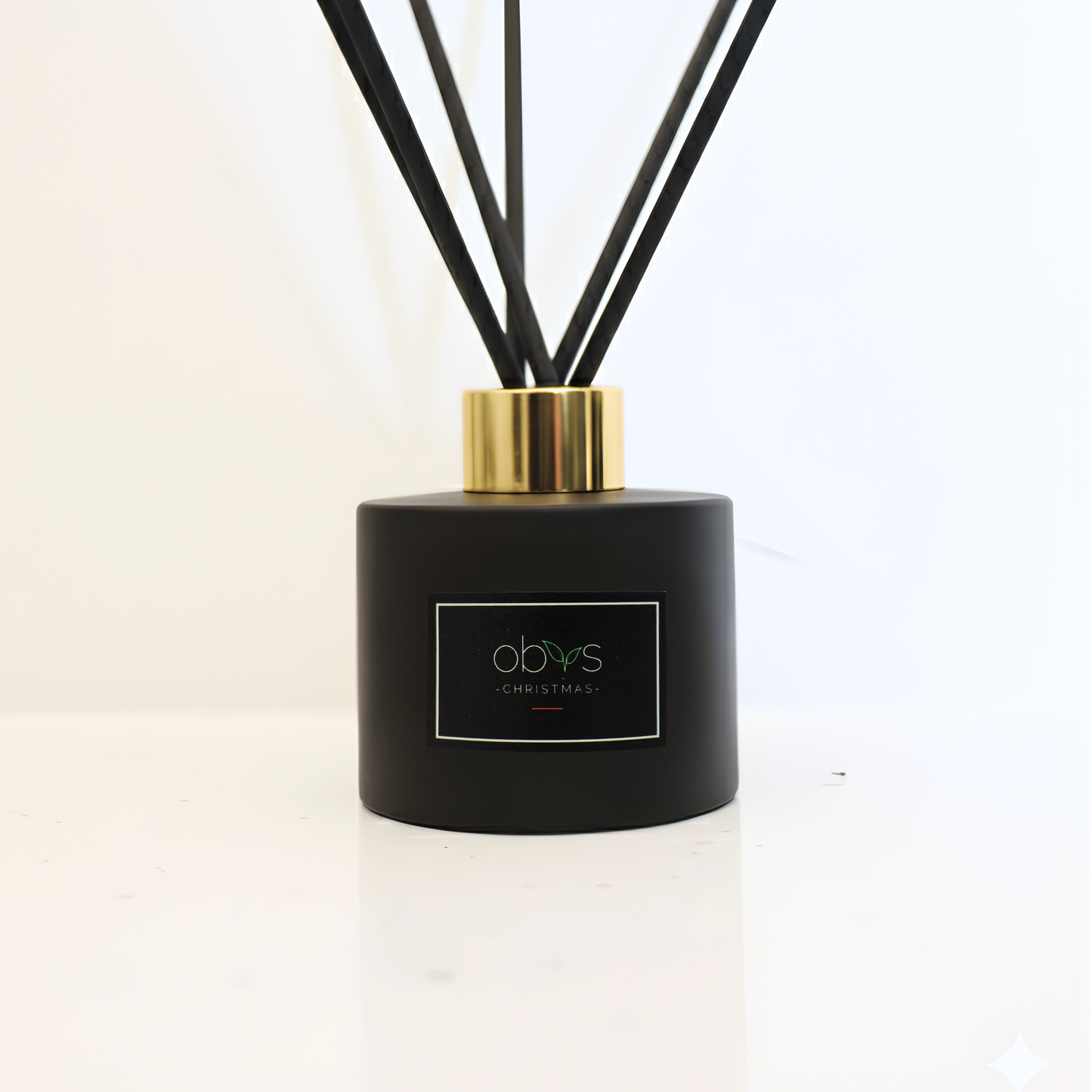 Black diffuser with gold cap and visible brand logo on a white backgroundObvs Skincare Christmas Reed Diffuser with cinnamon, clove and ginger essential oils on a festive background