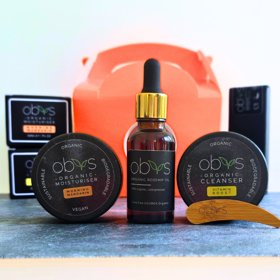 Flat lay of the Obvs Skincare Summer Glow Up Kit, including organic cleanser, citrus moisturiser, and rosehip oil, styled with summer flowers on a sunlit backdrop.